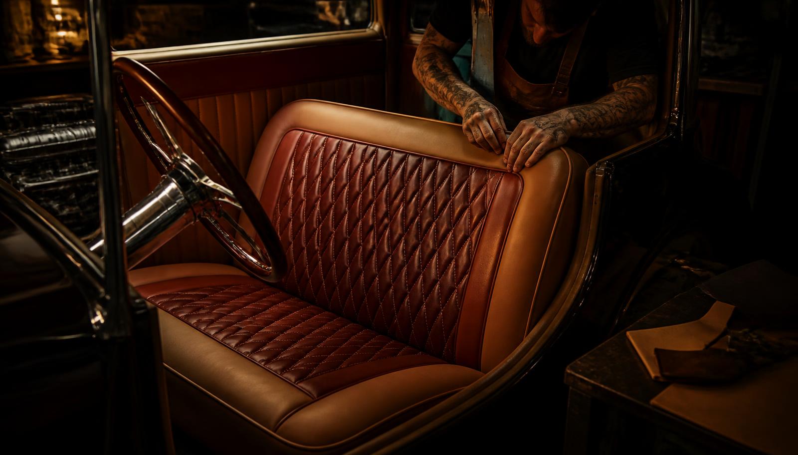 Trimmer fitting a diamond-stitched leather bench seat into a hot rod